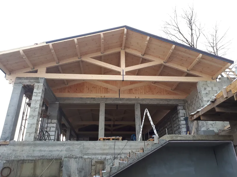 Șarpantă din lemn lamelar cu acoperiș în patru ape, montată peste o casă din cărămidă în construcție — LEMNER.MD