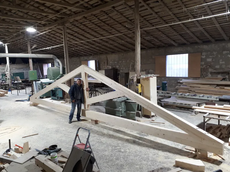 Șarpantă triunghiulară din grinzi de lemn lamelar asamblată în hala de producție, cu muncitor alături — LEMNER.MD
