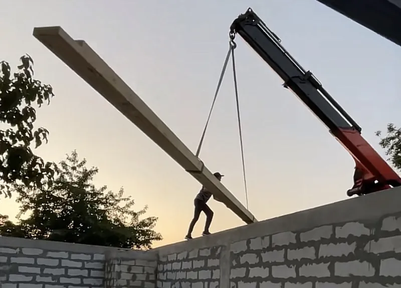 Grindă din lemn lamelar ridicată cu macaraua pe zidul unei case în construcție, cu muncitor pe șantier — LEMNER.MD