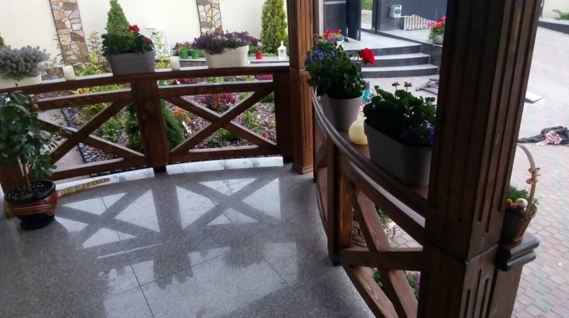 Terasă acoperită din lemn cu balustradă în X și stâlpi, cu jardiniere de flori, pe pavaj lângă casă — LEMNER.MD