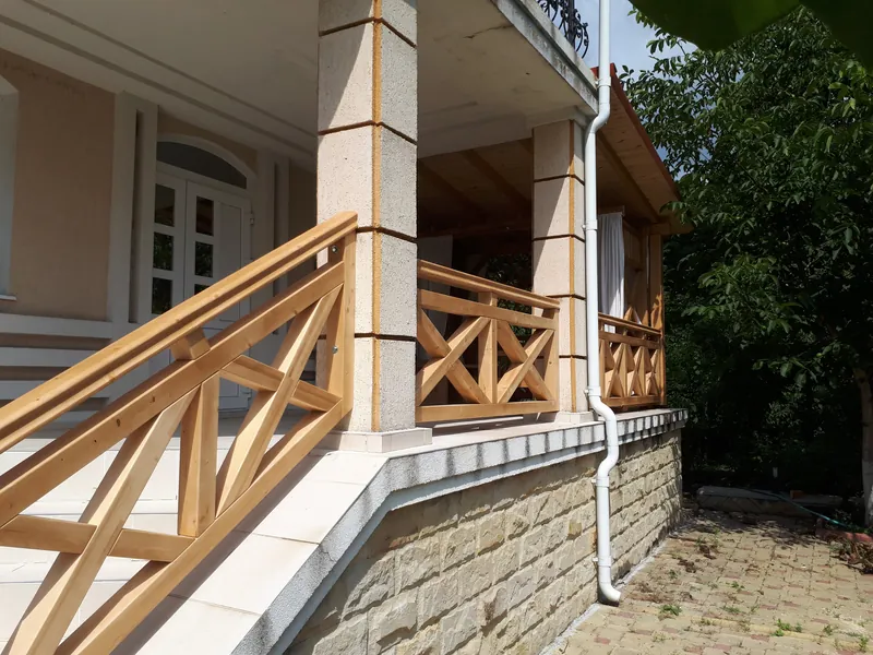 Terasă acoperită din lemn cu balustradă în X, scară cu balustradă din lemn și stâlpi placați cu piatră, lângă casă — LEMNER.MD