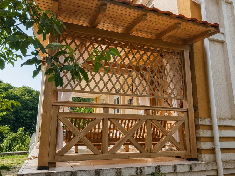 Foișor din lemn cu pereți din zăbrele traforate și balustradă în X, cu acoperiș din țiglă, lângă casă — LEMNER.MD