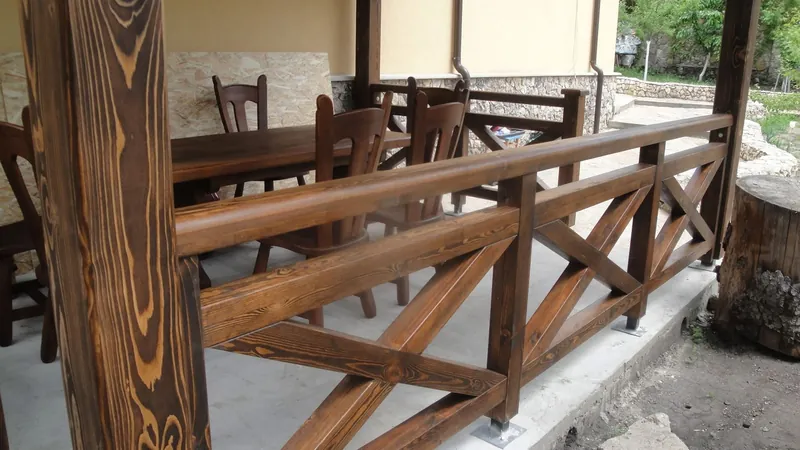Terasă acoperită din lemn cu balustradă în X și stâlpi masivi, cu masă și scaune, lângă casă — LEMNER.MD