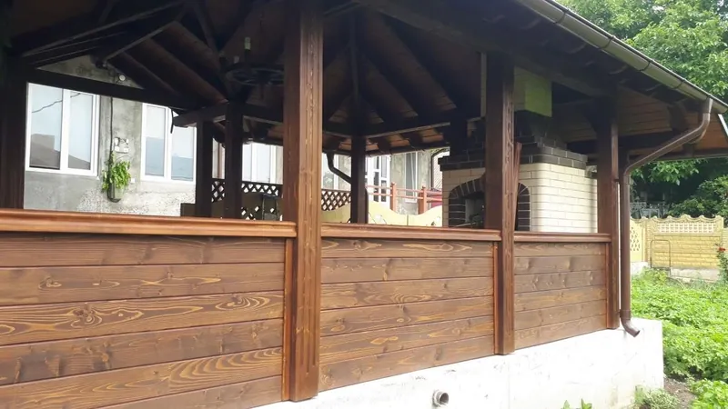 Terasă acoperită din lemn cu pereți închiși din scânduri orizontale și stâlpi, lângă casă, în grădină — LEMNER.MD