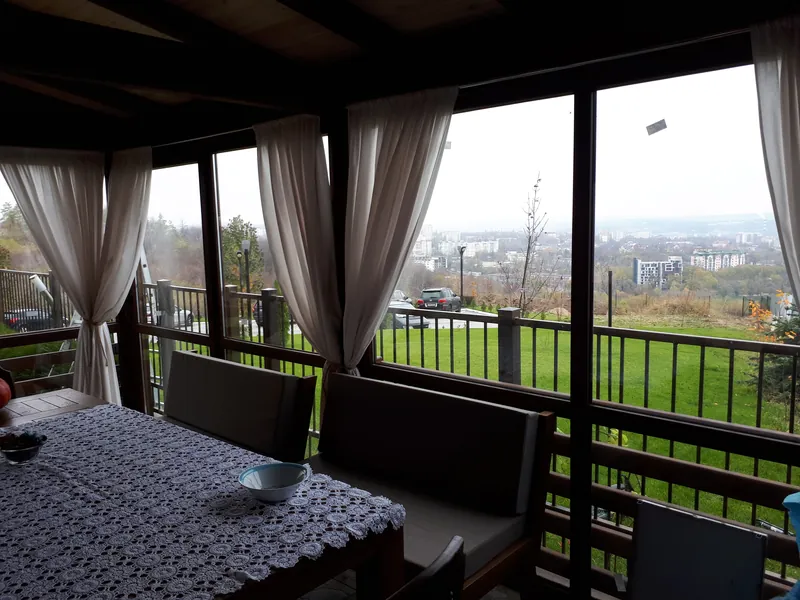 Interior de foișor închis din lemn, cu pereți de sticlă, draperii albe și masă, cu vedere panoramică spre vale — LEMNER.MD