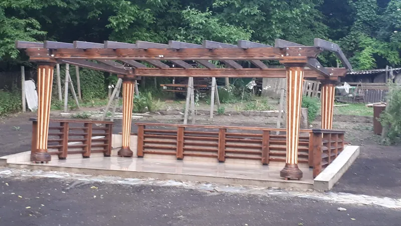 Pergolă din lemn cu stâlpi rotunzi canelați și balustradă, pe platformă pavată, în construcție — LEMNER.MD