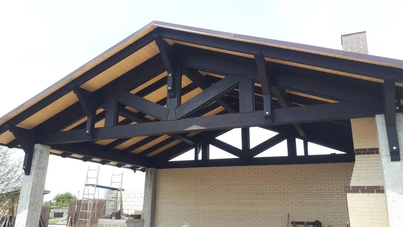 Structura din grinzi negre de lemn a acoperișului unei copertine, vedere de jos, lângă casă — LEMNER.MD