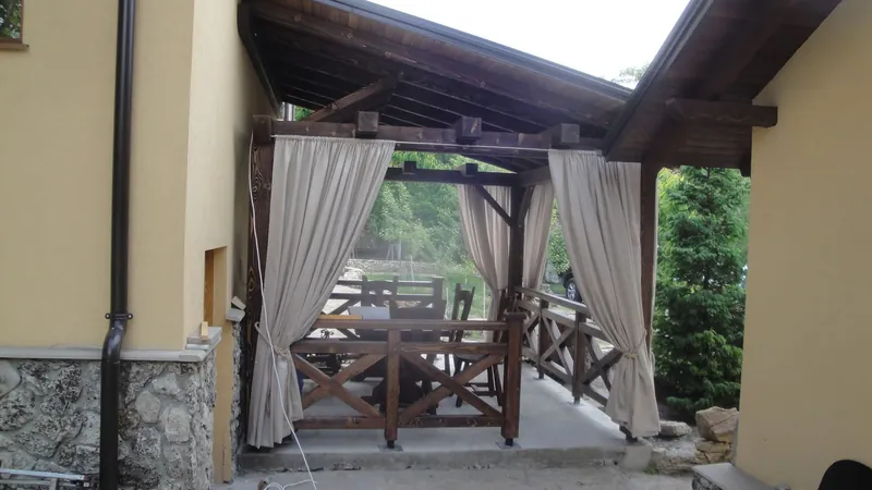 Foișor din lemn cu draperii bej, masă și bănci, alipit casei, cu balustradă în X — LEMNER.MD