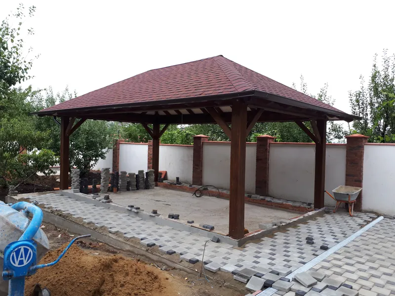 Foișor mare din lemn cu acoperiș în patru ape din șindrilă maro, lângă un gard cu stâlpi din cărămidă, pe o terasă pavată în construcție — LEMNER.MD