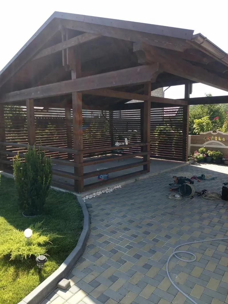 Foișor din lemn cu acoperiș în două ape și panouri laterale din șipci, pe o terasă pavată — LEMNER.MD