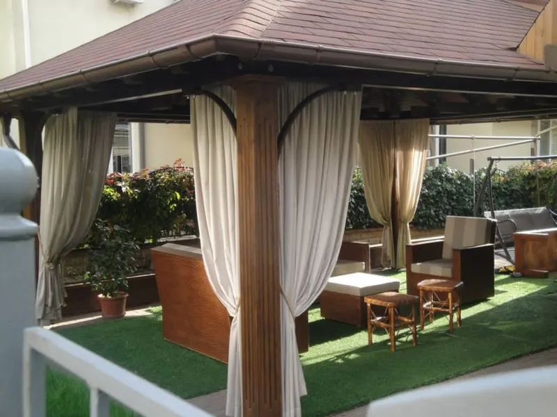 Foișor din lemn cu draperii bej, pe gazon, cu mobilier de relaxare — LEMNER.MD