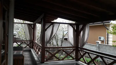 Terasă acoperită din lemn cu draperii și balustradă în X, cu vedere spre grădină primăvara — LEMNER.MD