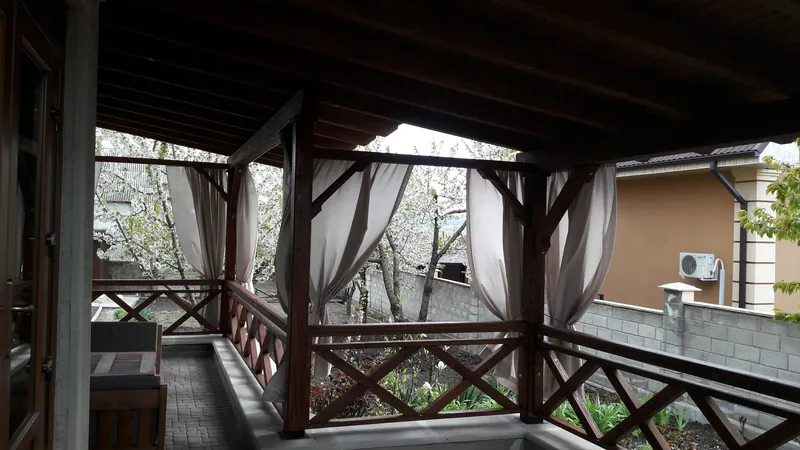 Terasă acoperită din lemn cu draperii și balustradă în X, cu vedere spre grădină primăvara — LEMNER.MD