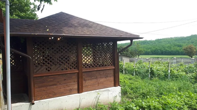 Foișor din lemn cu acoperiș în patru ape și panouri din zăbrele, cu vedere spre o vie — LEMNER.MD