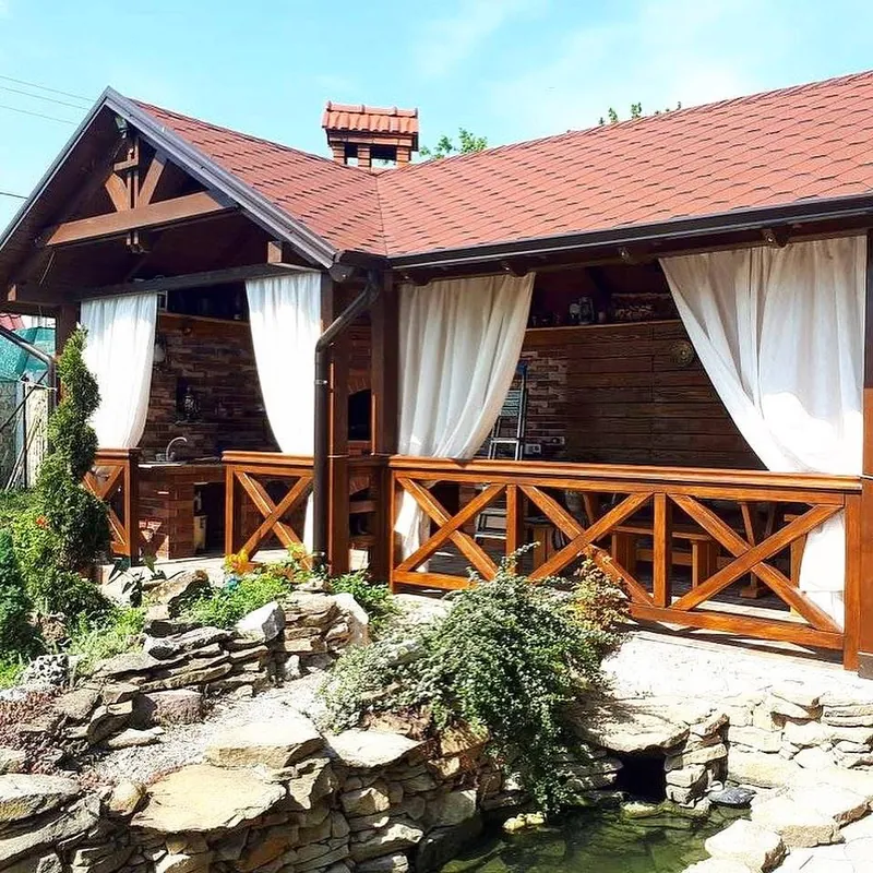 Foișor mare din lemn cu acoperiș în patru ape din țiglă roșie și draperii albe, lângă un iaz cu piatră — LEMNER.MD