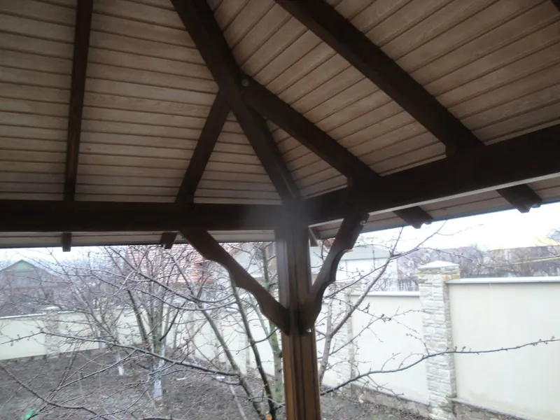Tavanul în patru ape din scânduri și grinzi al unui foișor, vedere de jos spre grădină — LEMNER.MD