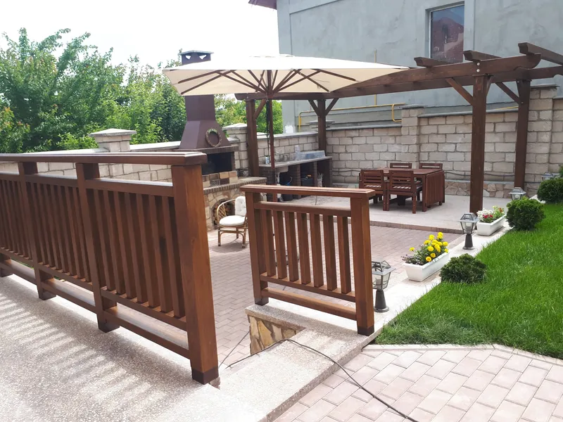 Curte amenajată cu balustradă din lemn, pergolă și zonă de grătar din cărămidă cu umbrelă — LEMNER.MD