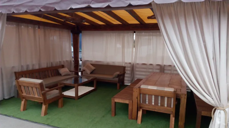 Set de lounge din lemn cu canapele și masă joasă, sub un foișor cu draperii, pe gazon — LEMNER.MD