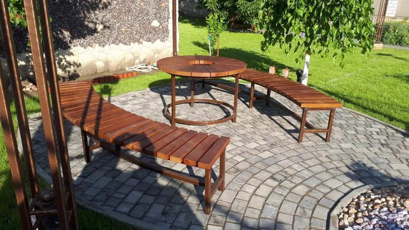 Masă rotundă din lemn cu bănci curbate în jurul ei, pe terasă pavată, în grădină — LEMNER.MD