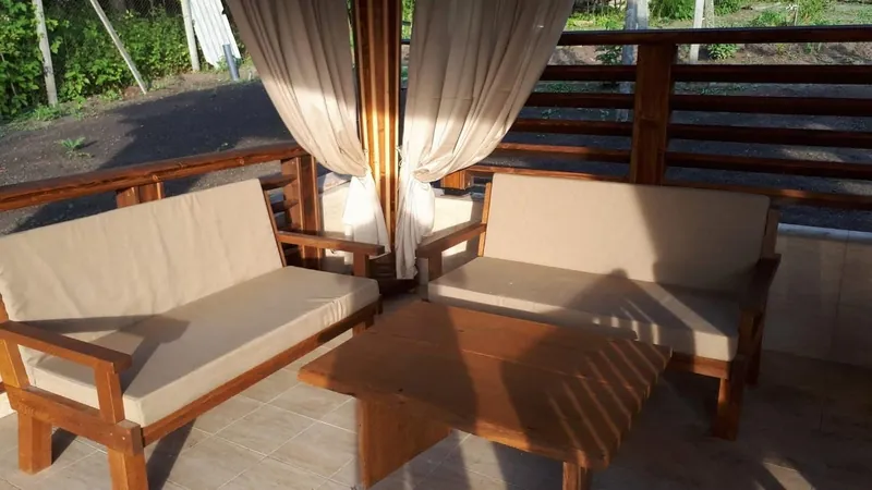 Două canapele din lemn cu perne bej, sub un foișor cu draperie, la lumina soarelui — LEMNER.MD