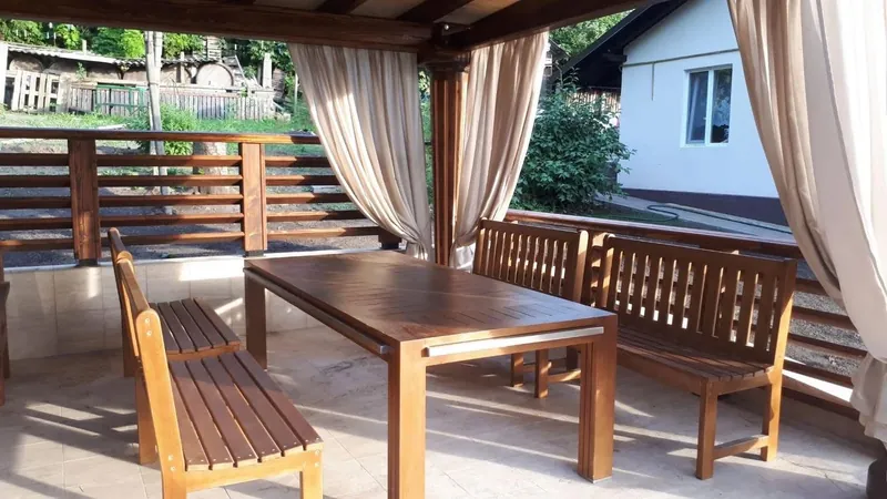 Masă din lemn cu două bănci, sub un foișor cu draperii, pe terasă pavată — LEMNER.MD
