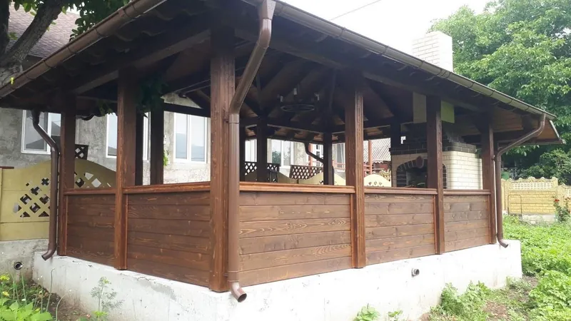 Foișor din lemn cu acoperiș în patru ape și zonă de grătar, cu balustradă din scânduri, într-o curte — LEMNER.MD