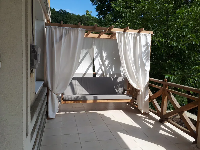 Leagăn din lemn în cadru pergolă cu laterale în X, copertină în dungi și pernă bej, pe gazon — LEMNER.MD